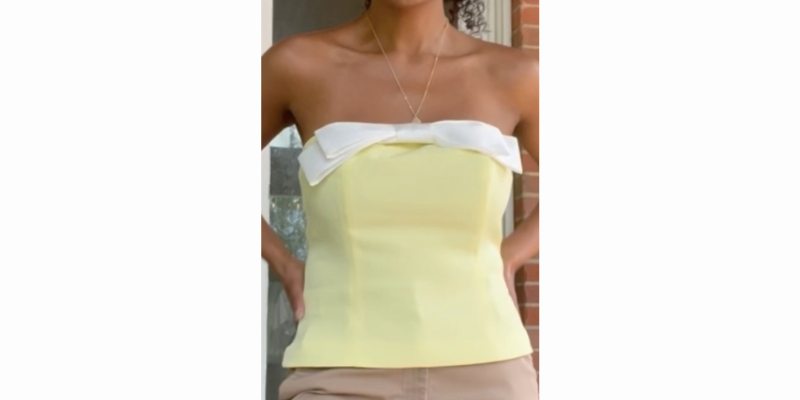 woman posing in a strapless tube top, it is buttery yellow with a white bow on the top of the shirt